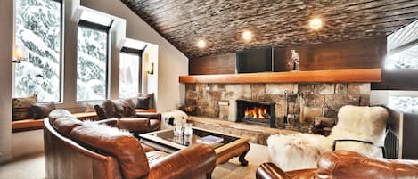 Comfortable seating in leather couch and armchair, mantle mounted smart TV over the wood burning fireplace