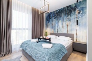 A modern bedroom with decorative wallpaper on the wall behind the bed headboard adds a unique touch of style. Soft curtains in the windows give the room a light and cosy feel.