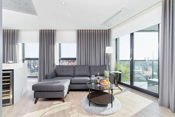 Modern, spacious living room with grey sofa with coffee table. The room has panoramic windows that let in plenty of natural light.