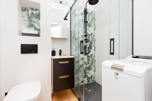 Bathroom with a shower, toilet, sink with mirror and washing machine.