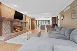 Open concept living room with TV and fireplace extends into the kitchen.