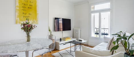 Acogedor salón con sofá, balcón francés, smart TV y mesa para hasta 4 comensales