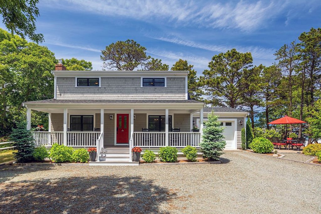 A two story vacation home in Provincetown, Massachusetts is seen with a spacious front porch and a covered patio on a sunny summer day.