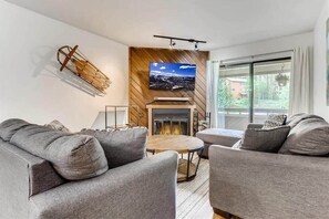 Relax in the living room with a plush L-shaped sofa, a cozy love seat, indoor wood fireplace, flat-screen TV, and access to the private outdoor balcony