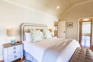 The master bedroom features a king bed, night stands with reading lamps and vaulted shiplap ceilings.