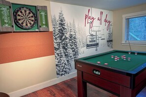 The open living and game area downstairs with 3 arcade games, flat screen tv, bumper pool, darts, Hook 21, and shot ski (21+). It is connected to kitchenette area. 
