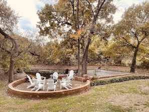 Outdoor wood fire pit under string lights next to the pond