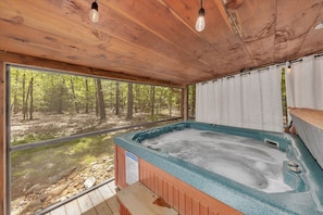 Six person hot tub on the screened in back porch overlooking forest land.