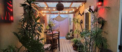 Outdoor covered patio w/ lots of plants and a table + chairs.