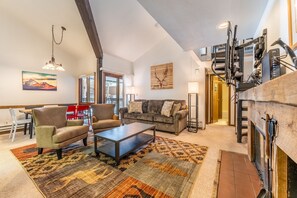 Spacious living area with mounted flat screen TV, wood-burning fireplace, vaulted ceilings, sleeper sofa and access to the private deck.