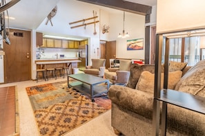 Spacious living area with mounted flat screen TV, wood-burning fireplace, vaulted ceilings, sleeper sofa and access to the private deck.