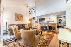Spacious living area with mounted flat screen TV, wood-burning fireplace, vaulted ceilings, sleeper sofa and access to the private deck.