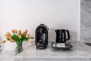 A compact kitchen corner with a coffee maker, kettle, and fresh tulips adding a vibrant touch.
