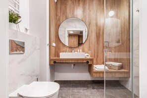 A stylish bathroom with a round mirror, wood accents, and clean white tiles.
