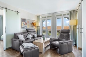 Wohnbereich mit Sofa, Sessel, Couchtisch und Zugang zum Balkon