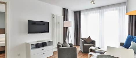 Wohn-Essbereich mit Couch, Flatscreen TV, Esstisch, Sitzgelegenheit und Zugang zum Balkon