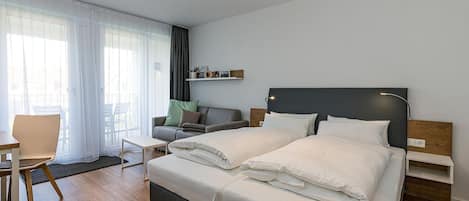 Wohn-Ess-Schlafbereich mit Sofa, Esstisch, Sitzgelegenheit und Doppelbett sowie Zugang zum Balkon