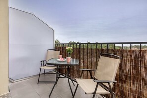 A balcony with a table and two chairs, overlooking the lush green landscape. Perfect for outdoor relaxation with privacy fencing.