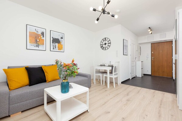 A bright living room with a comfortable sofa, vibrant cushions, and a modern dining table.
