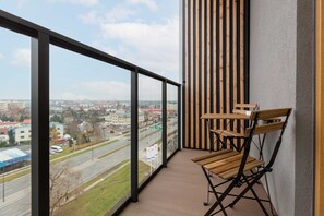 A private balcony with a small table and chairs, offering a view of the cityscape and greenery.

