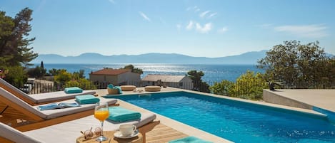 Sunbathing area with deck chairs by private pool in modern luxury villa Azul in Makarska for vacation and rent.