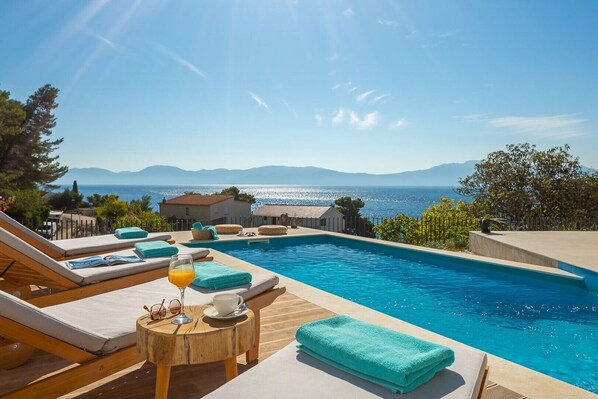 Sunbathing area with deck chairs by private pool in modern luxury villa Azul in Makarska for vacation and rent.