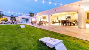 Large open backyard grass area w/ cornhole, string lights, & covered patio