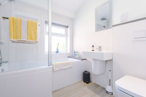 Bathroom with L shaped bath, overhead rain shower, floating sink and toiletries
