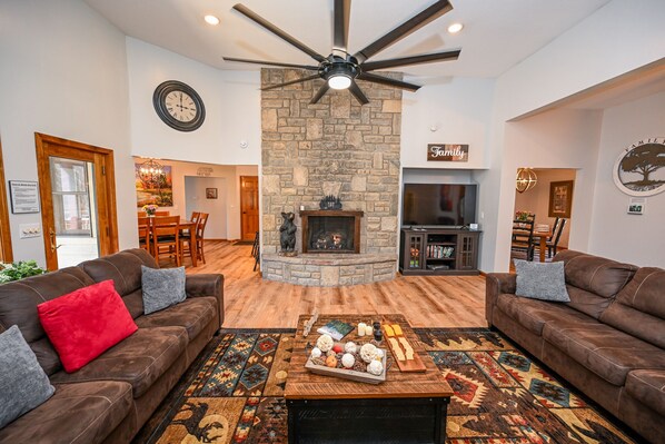 Large great room with stone fireplace, three large sofas, and access to deck