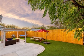 Discover a small, cozy backyard retreat, complete with lush greenery, comfortable seating, and ambient lighting.