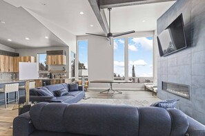 Relax in this modern and spacious family room with luxurious sofa seating, a built-in fireplace, a flat-screen TV, and expansive floor-to-ceiling windows throughout the space