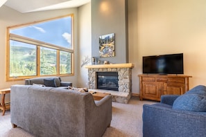 Living area with new furnishings, Smart TV, vaulted ceilings, and a gas fireplace with beautiful stone surround.