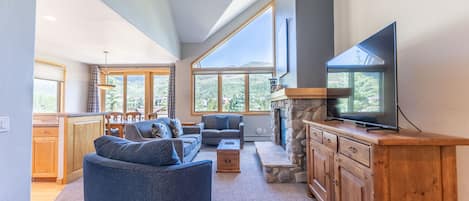 Living area with new furnishings, Smart TV, vaulted ceilings, and a gas fireplace with beautiful stone surround.