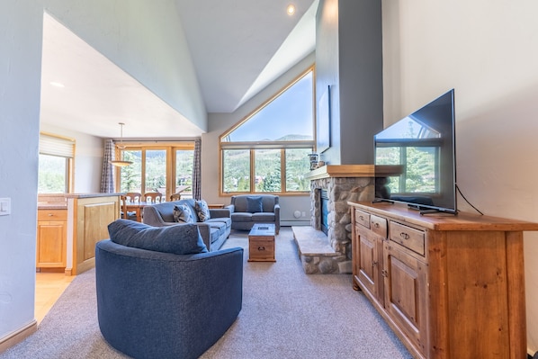 Living area with new furnishings, Smart TV, vaulted ceilings, and a gas fireplace with beautiful stone surround.