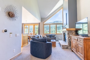 Living area with new furnishings, Smart TV, vaulted ceilings, and a gas fireplace with beautiful stone surround.