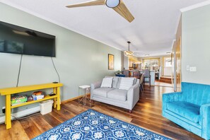 Main level living area with mounted flat screen smart TV, hardwood flooring, ample seating and access to the private deck.