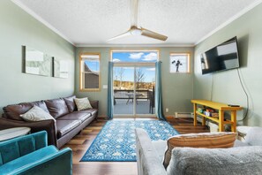 Main level living area with mounted flat screen smart TV, hardwood flooring, ample seating and access to the private deck.