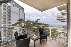 A modern balcony with cozy chairs and a small table, perfect for enjoying fresh air while overlooking lush greenery.