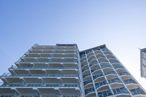 The exterior of a modern building with large balconies and a contemporary design, reaching up towards a clear, blue sky.