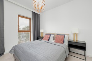 A cozy bedroom with soft gray bedding and decorative pillows, accented by a stylish bedside table and modern lighting.
