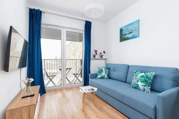 A modern living room featuring a blue sofa, a wooden coffee table, and a small balcony visible through glass doors.