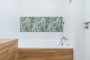 A clean and minimalistic bathroom featuring a bathtub, white tiles, and a wooden cabinet.