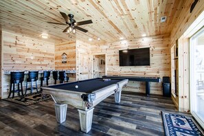 Cozy game room with pool table, bar seating, and large TV.