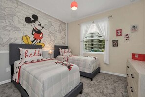 Mickey Mouse-themed guest room with two twin beds, a TV, and access to a shared bathroom.
