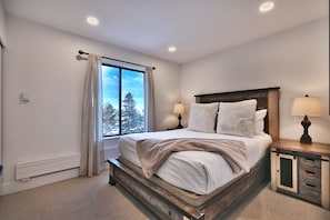 Main bedroom with queen bed and wooden bedframe with large picture window