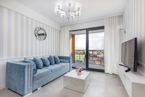 A bright living room featuring a light blue sofa, a white coffee table, and a large window allowing natural light to fill the space.