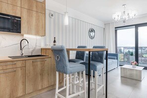 A compact kitchen area with light wooden cabinets, a marble backsplash, and blue upholstered bar stools at a breakfast bar.