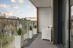 A modern balcony with a railing, potted plants, and a view of greenery and residential buildings in the distance.