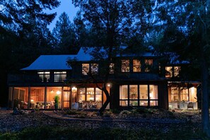 The house glows warmly against the night sky, with softly lit windows and outdoor lights creating a cozy, inviting atmosphere.