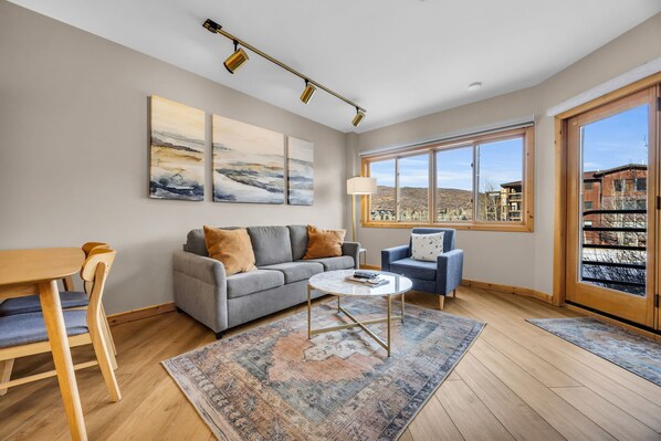 Relax in the natural light filled living room with a plush sofa, armchair seating, a cozy indoor wood fireplace, a flat-screen TV, and access to the private outdoor patio.